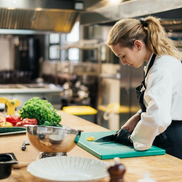widok-z-boku-kobiety-szefa-kuchni-w-rekawicy-krojenia-warzyw-w-kuchni